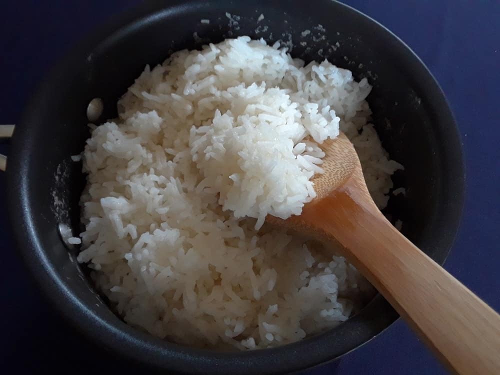 The cooked rice is fluffed and cooled with a wooden spoon.