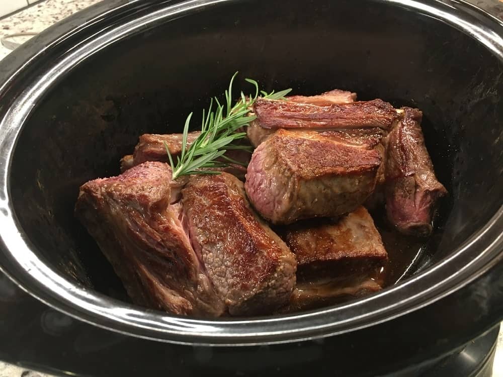 The browned pieces of short ribs are then transferred to the slow cooker along with herbs.