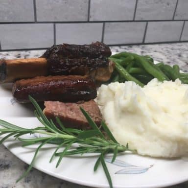 A freshly cooked plate of braised slow cooker short ribs with a side of mashed potatoes and steamed vegetables.