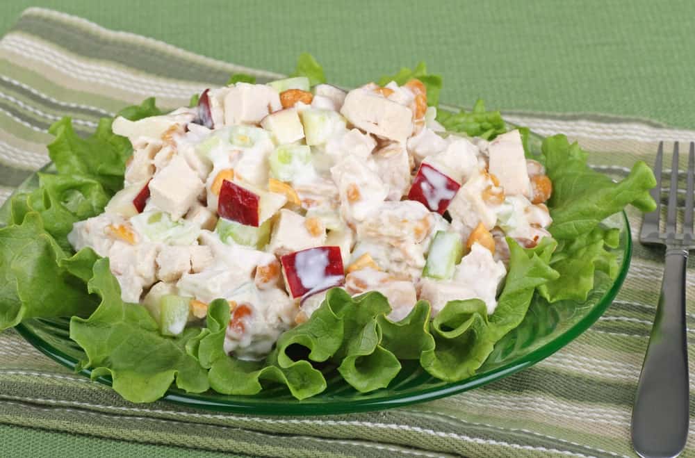 A plate of chicken salad with slices of apples and garnished with lettuce.