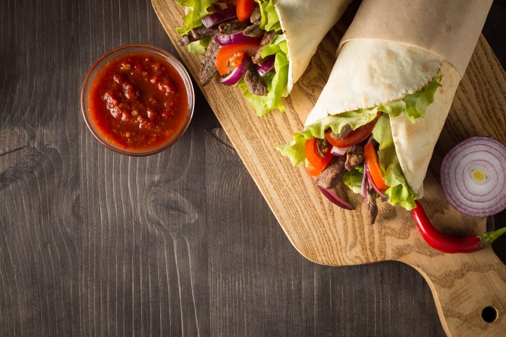 A pair of wrapped fajitas with a side of salsa.