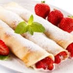A plate of strawberry cream cheese crepes with fresh strawberry on the side.