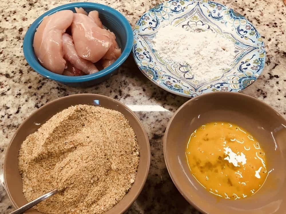 The ingredients in separate bowls for dipping the chicken breasts.