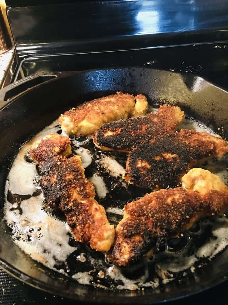 The pieces of breaded chicken breasts are fried on heated oil.