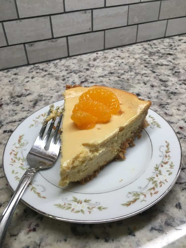 A slice of orange creamsicle cheesecake topped with fresh orange slices.