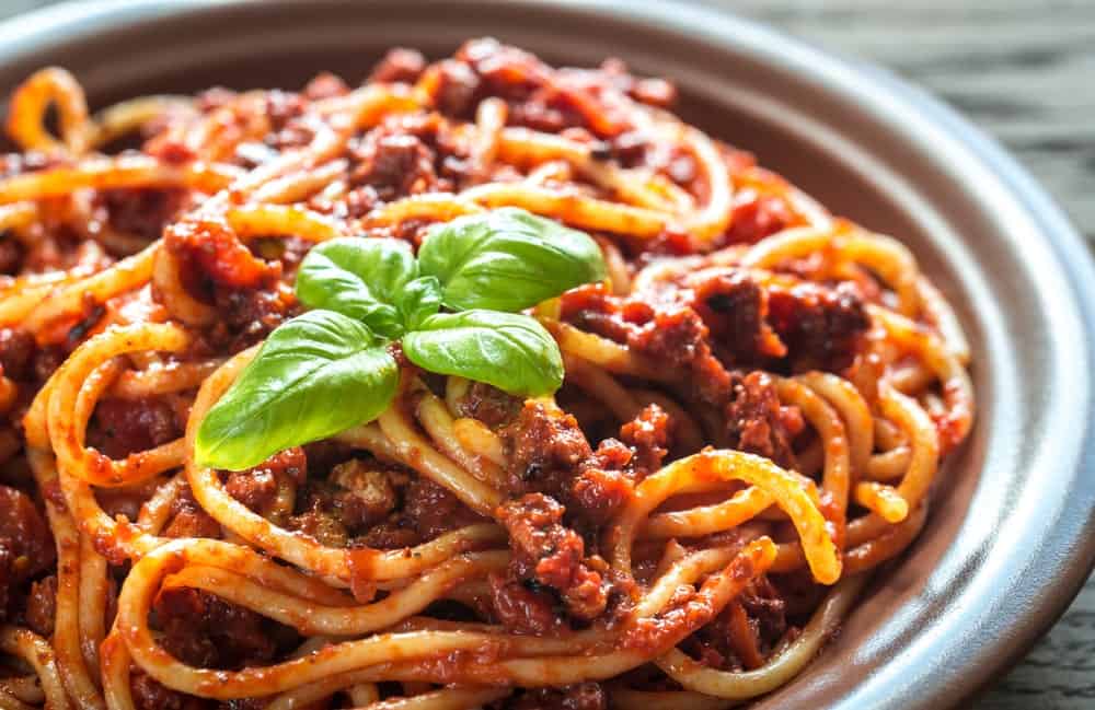 A close look at a plate of Bolognese pasta garnished with fresh basil leaves.