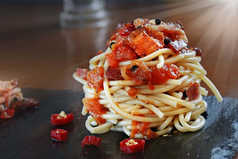 A close look at a serving of Amatriciana pasta with a generous topping of cured pork and chili.