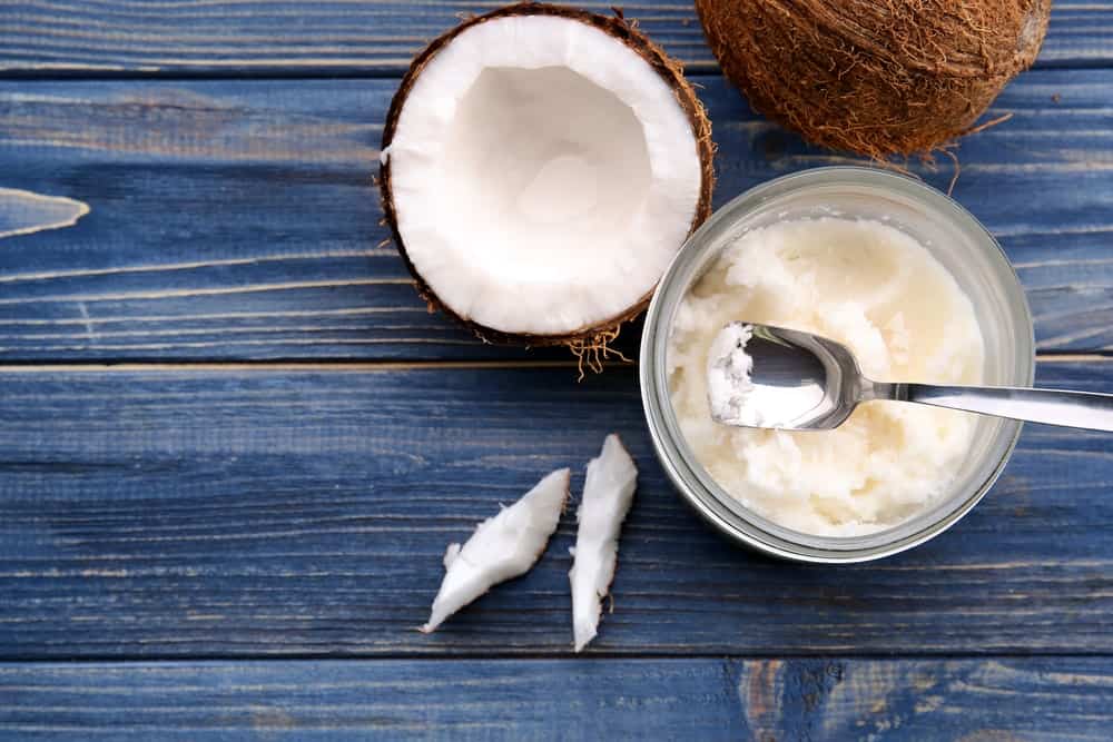 An opened jar coconut oil with fresh coconuts.