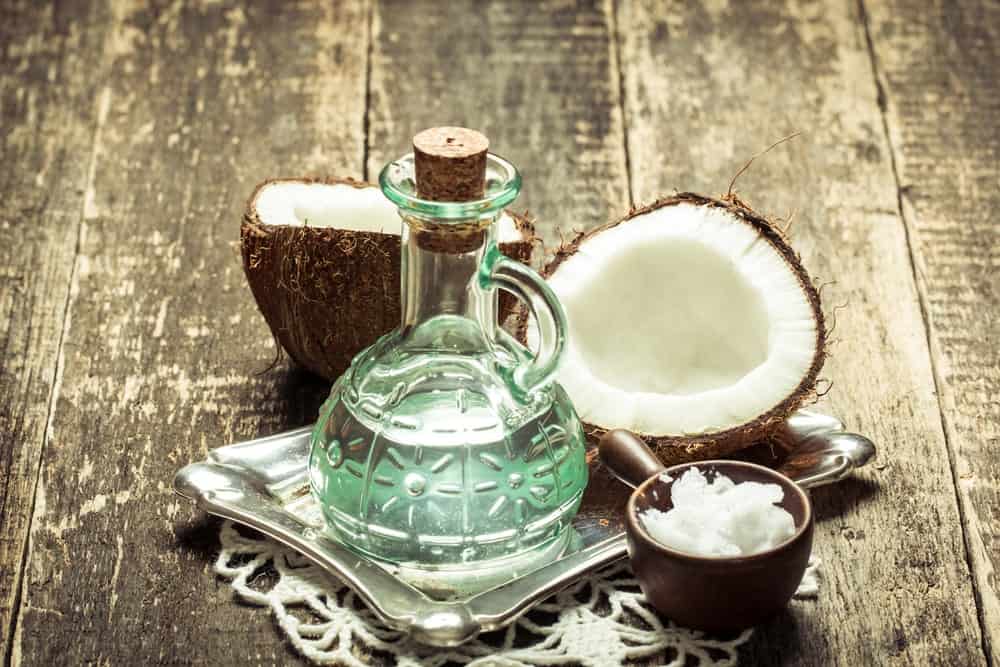 A glass bottle of coconut oil with fresh coconuts.