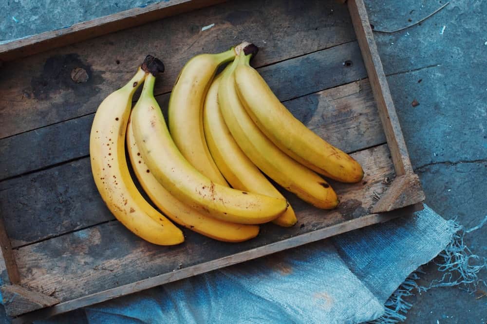 Clusters of ripe bananas on a wooden tray.