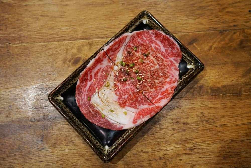 Premium raw thin sliced wagyu ribseye prepared for Japanese style barbecue on a black platter.