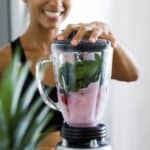 A woman is making a healthy blended smoothie with fruits and spinach.