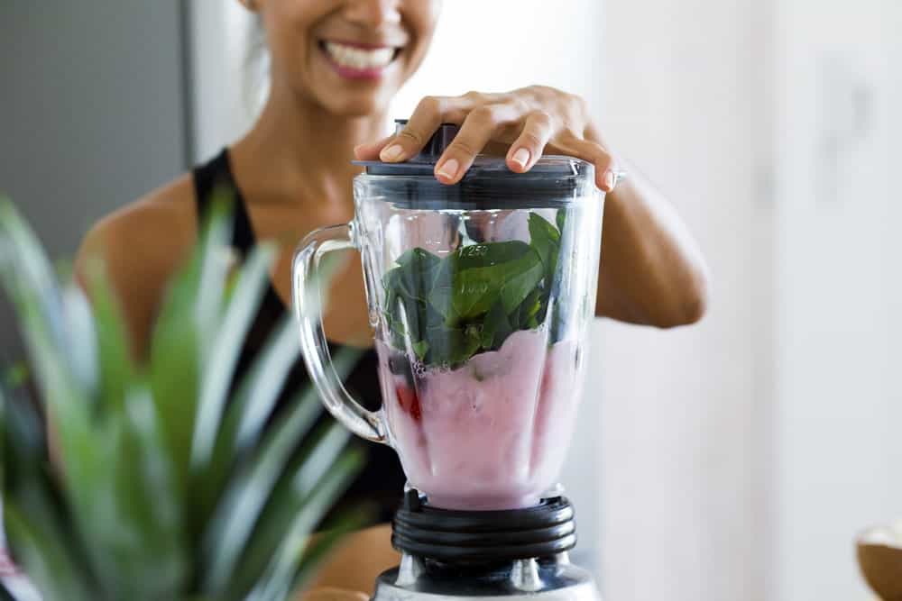 A woman is making a healthy blended smoothie with fruits and spinach.