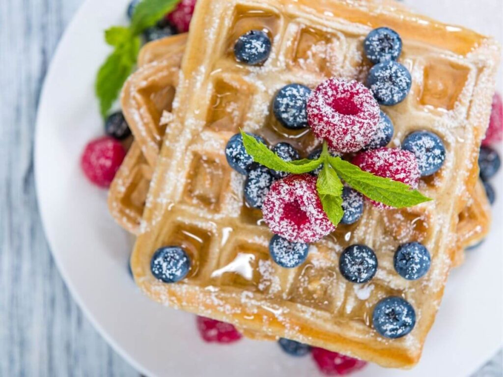 Freshly made Krusteaz Waffles with fruit and powdered sugar.