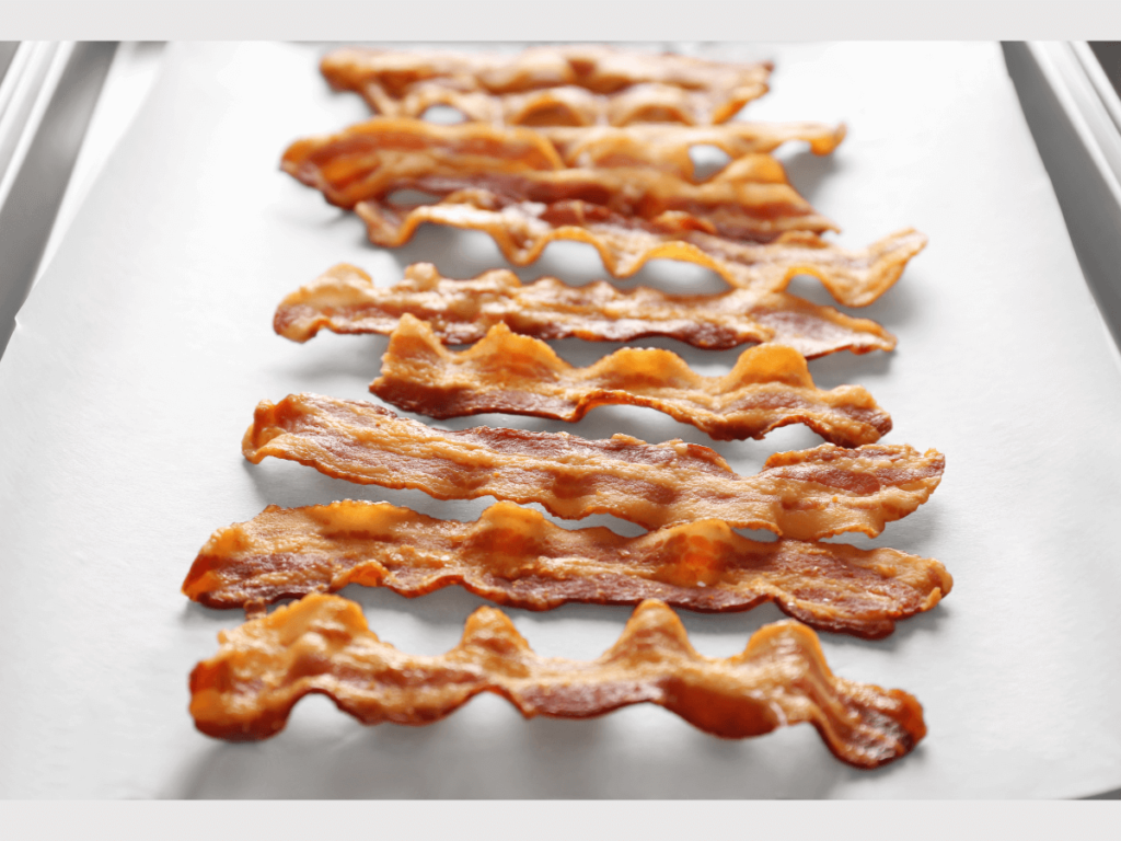 bacon being cooked on a baking sheet with parchment paper