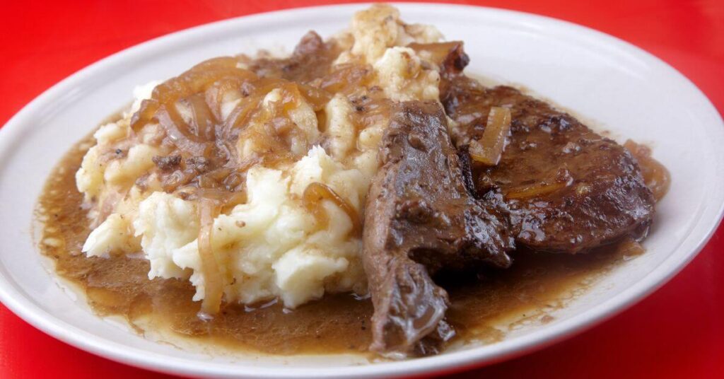 a plate of liver, onions and mashed potatoes