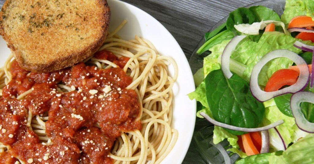 dish of spaghetti with salad and garlic bread