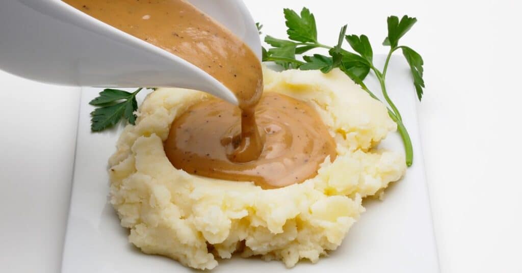 gravy in a gravy boat getting poured on mashed potatoes